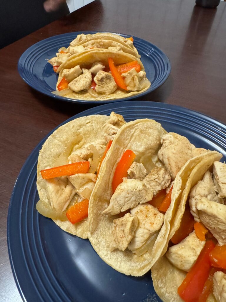 This image is a close up of the chicken fajitas. It is seasoned chicken chunks, grilled onion and bell peppers wrapped in corn tortillas.