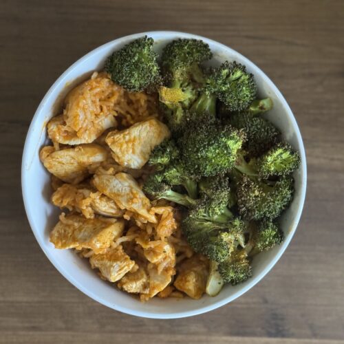 This is a picture of a curry dinner bowl. It has chopped chicken and rice covered in a simmer curry sauce served with roasted broccoli on the side.