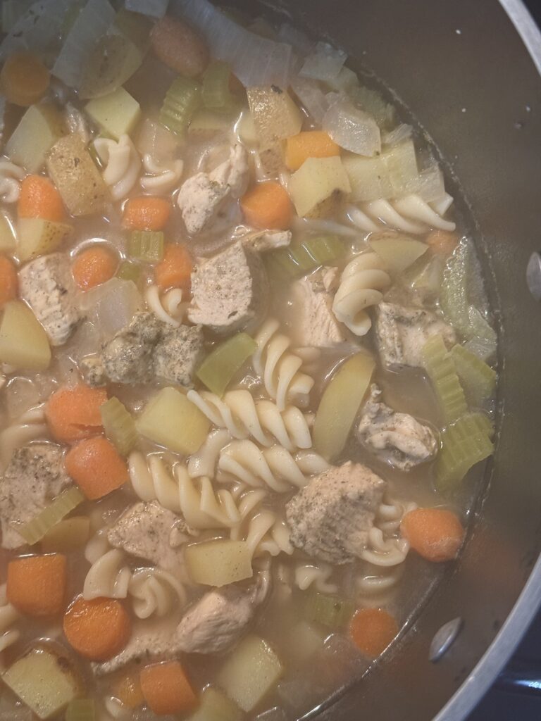 This is a close up of the gluten free chicken noodle soup. You can see the rotini pasta, potatoes, chicken, celery and carrots sitting in the broth.