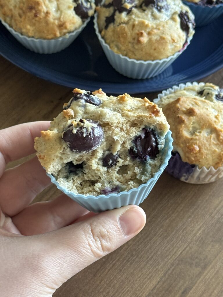 This image is a close up of 1 gluten free blueberry muffin. It has part of the top removed so you can see the juicy blueberries on the inside.